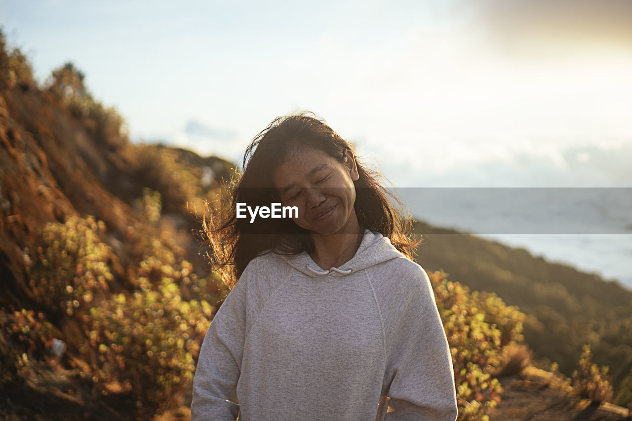 Smiling woman with eyes closed standing on mountain against sky