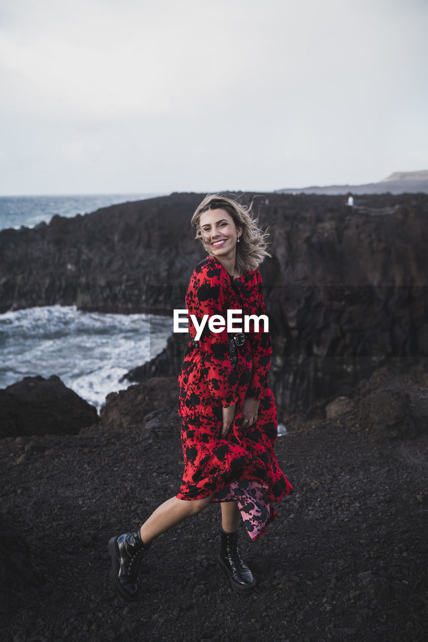 Young woman smiling while standing on mountain at los hervideros, lanzarote, spain