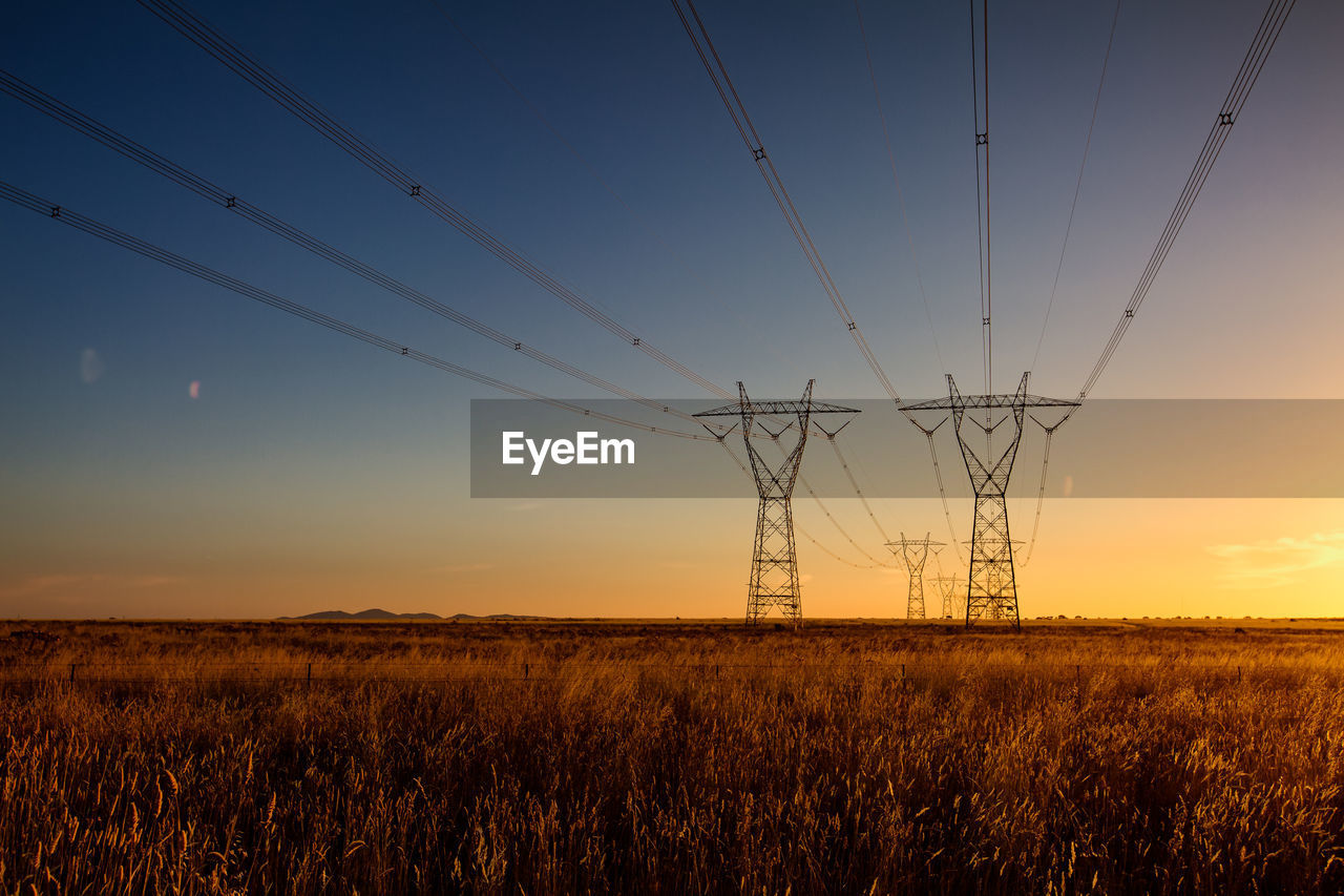 ELECTRICITY PYLON ON FIELD AGAINST SKY AT SUNSET