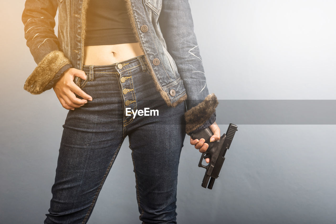 Midsection of woman holding handgun while standing by wall