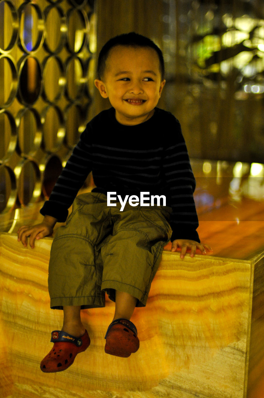 Smiling boy looking away while sitting on wooden structure