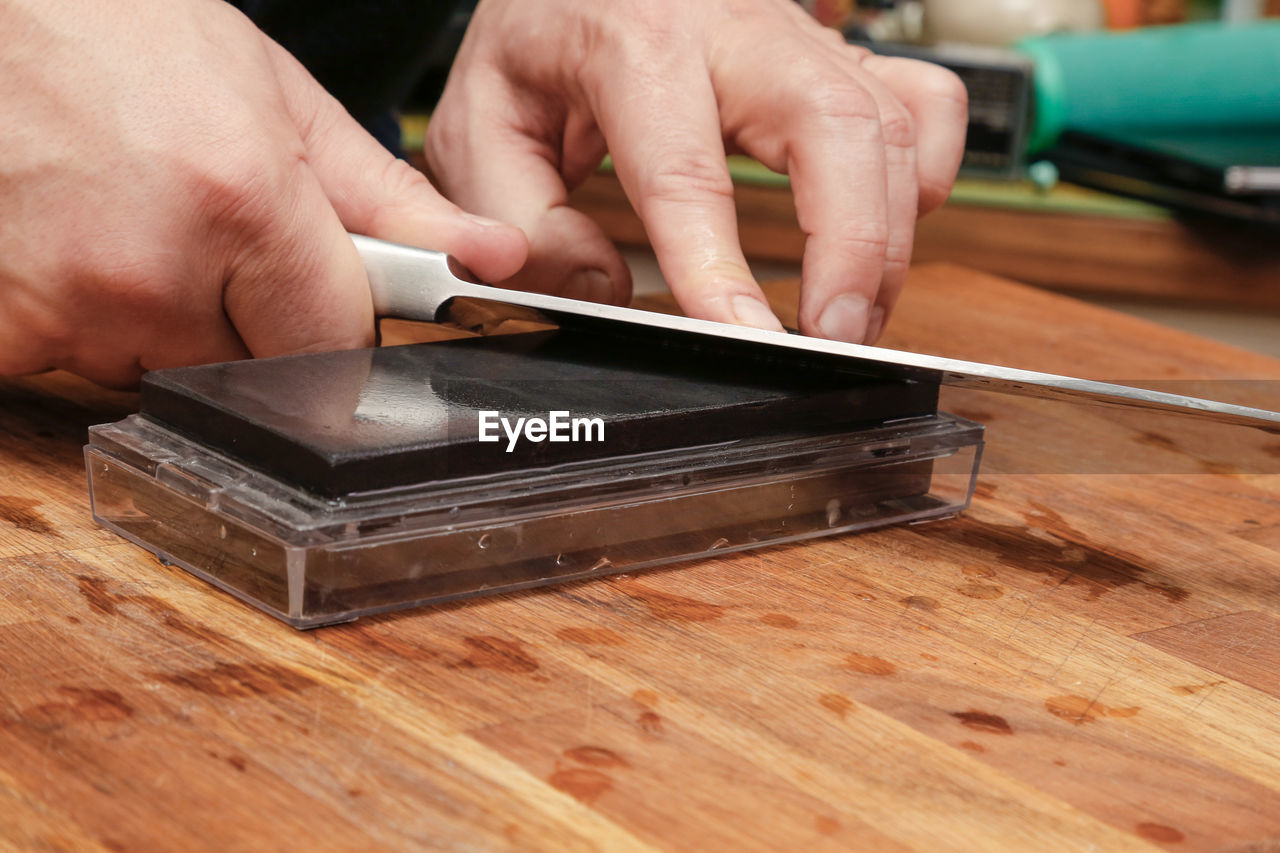 Cropped hand of person sharpening knife on table