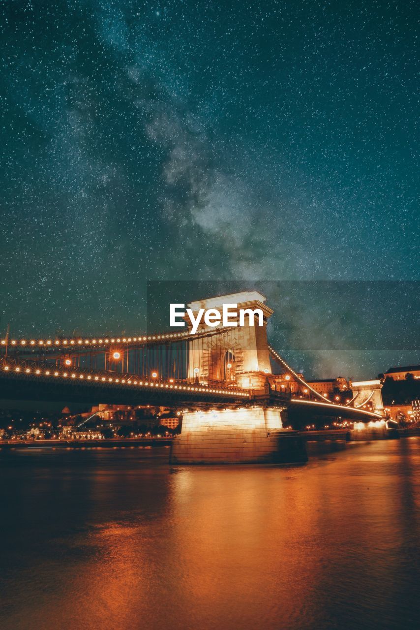 Illuminated bridge over river against sky at night