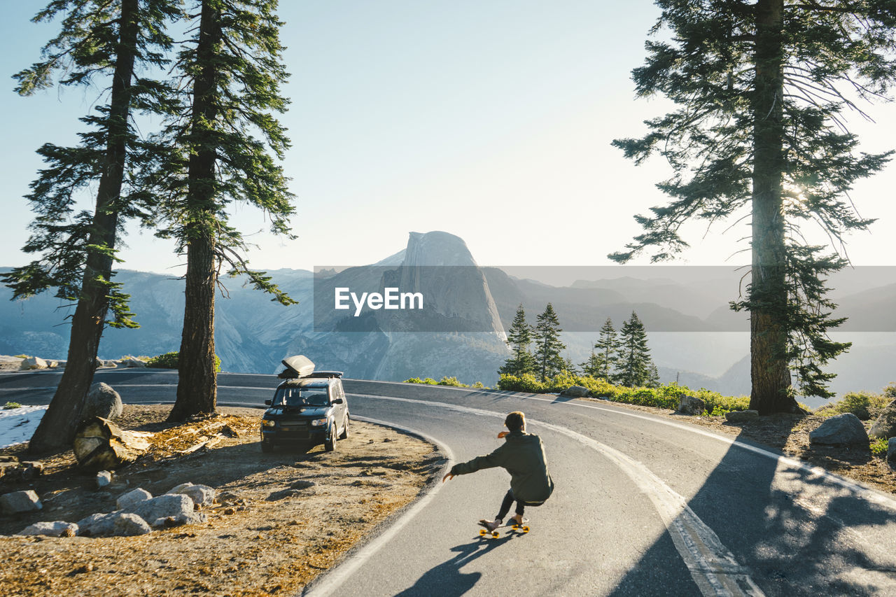 Rear view of man skateboarding on road by mountains against clear sky