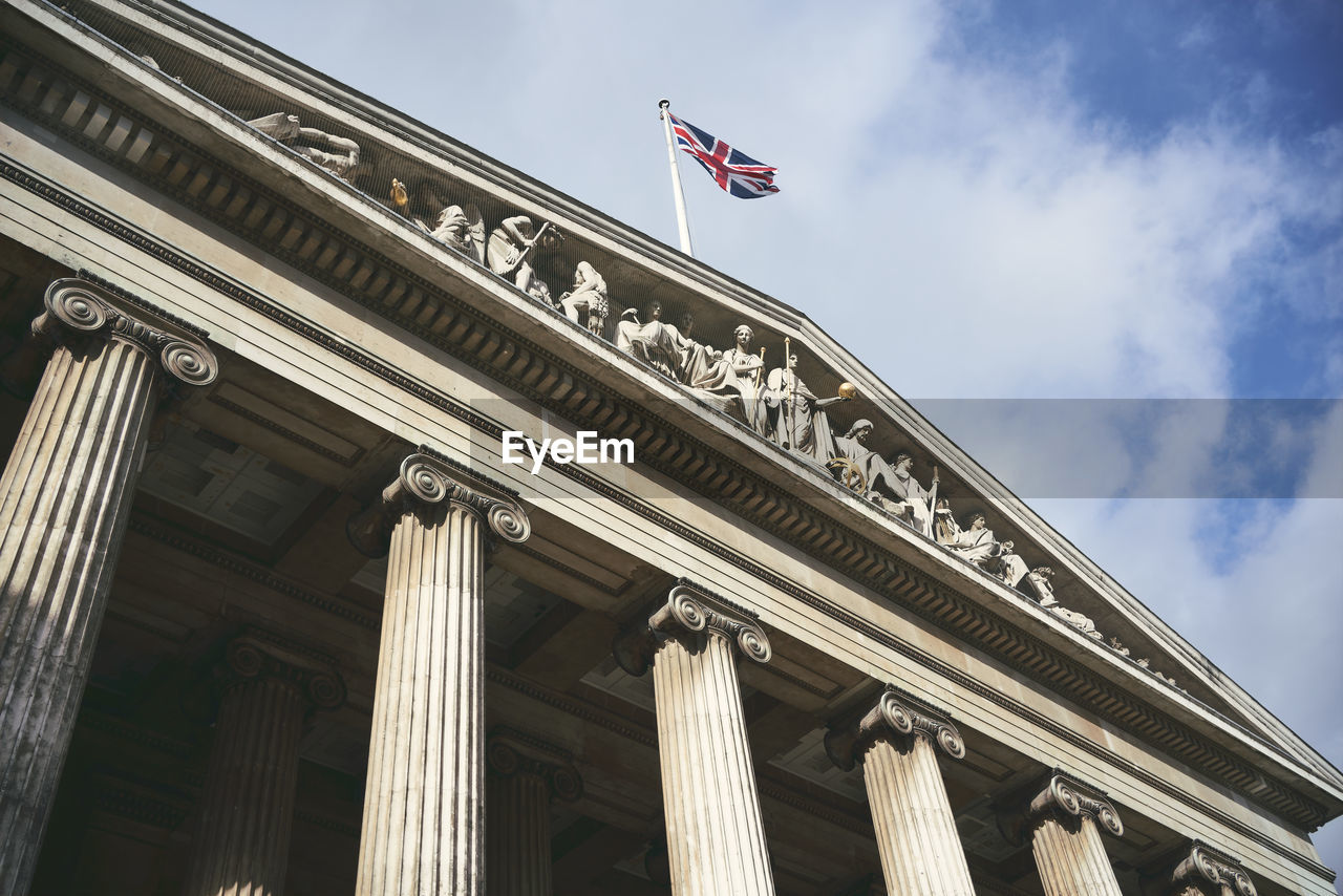 From below flag of great britain fluttering on top of aged ornamental building with columns against cloudy sky