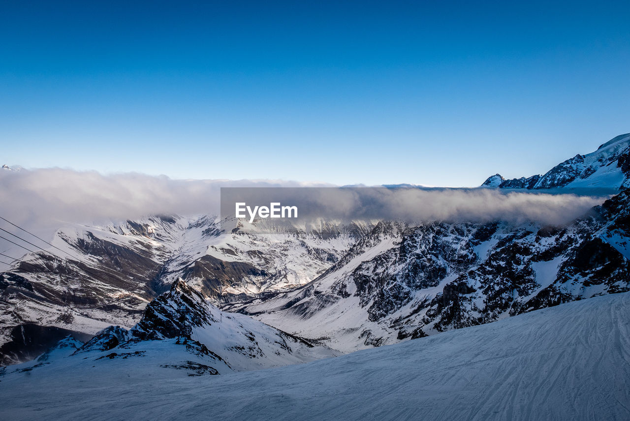 Scenic view of snow covered mountains against blue sky