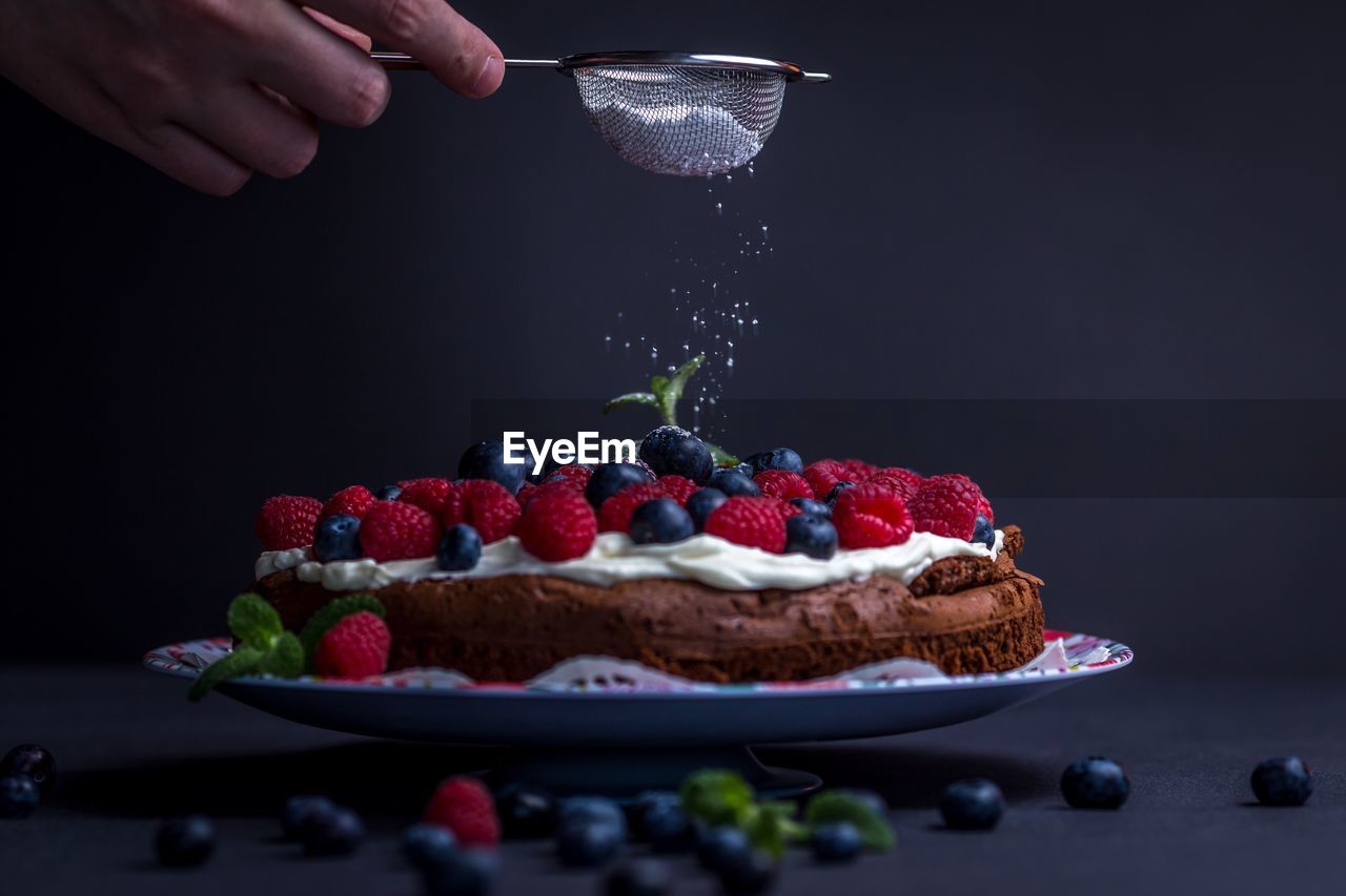 Cropped image of hand pouring powdered sugar into cake