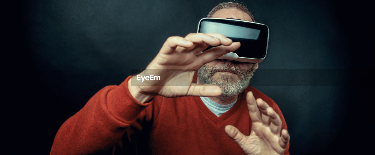 Panoramic view of senior man using virtual reality headset against black background