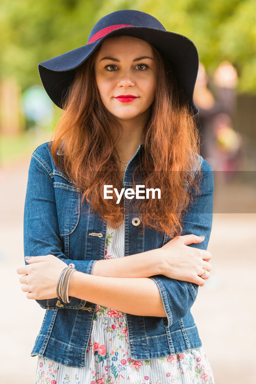 Portrait of beautiful woman in hat standing with arms crossed