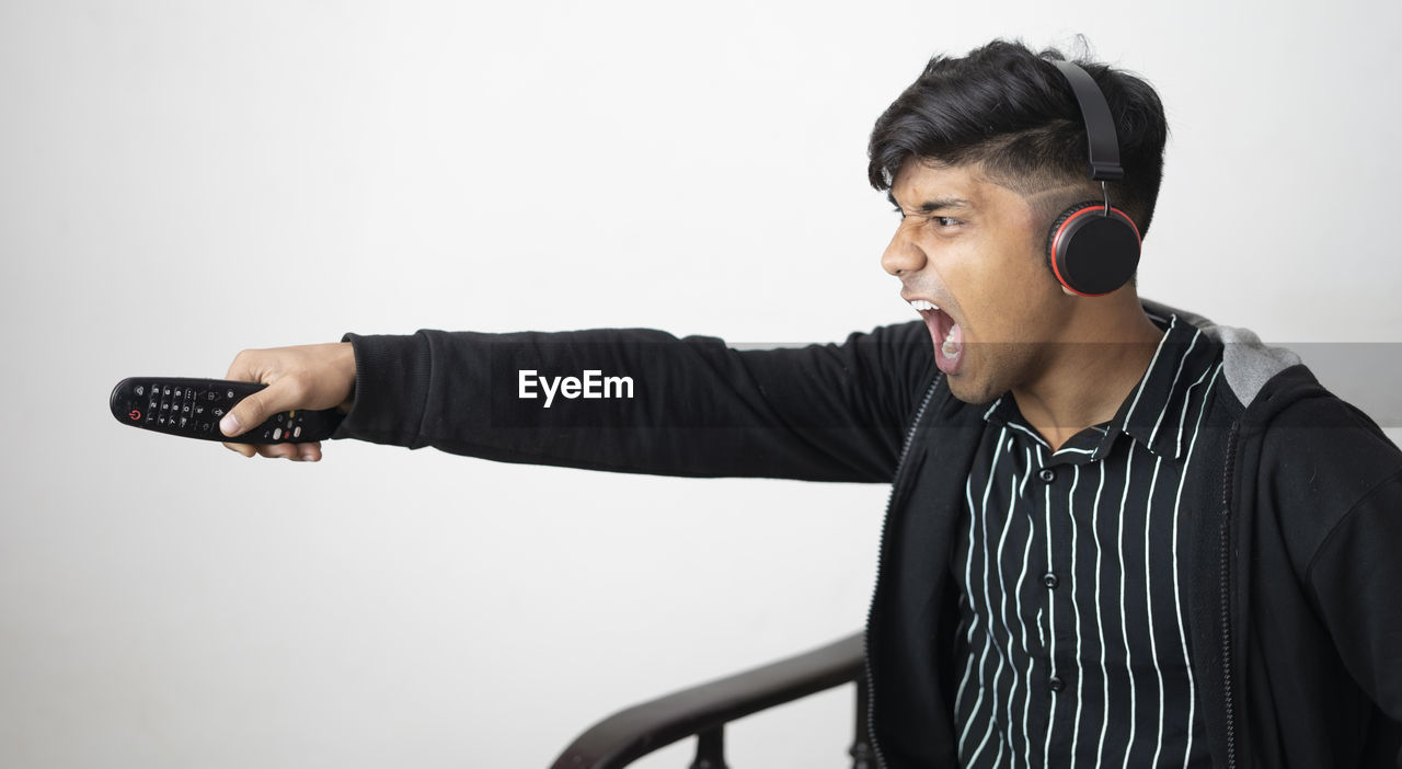 Asian man with headphone wearing black jacket holding remote excited to the match with arms raised.