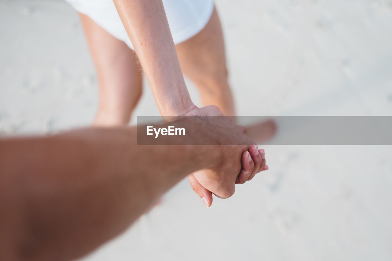Cropped image of couple holding hands while walking at beach