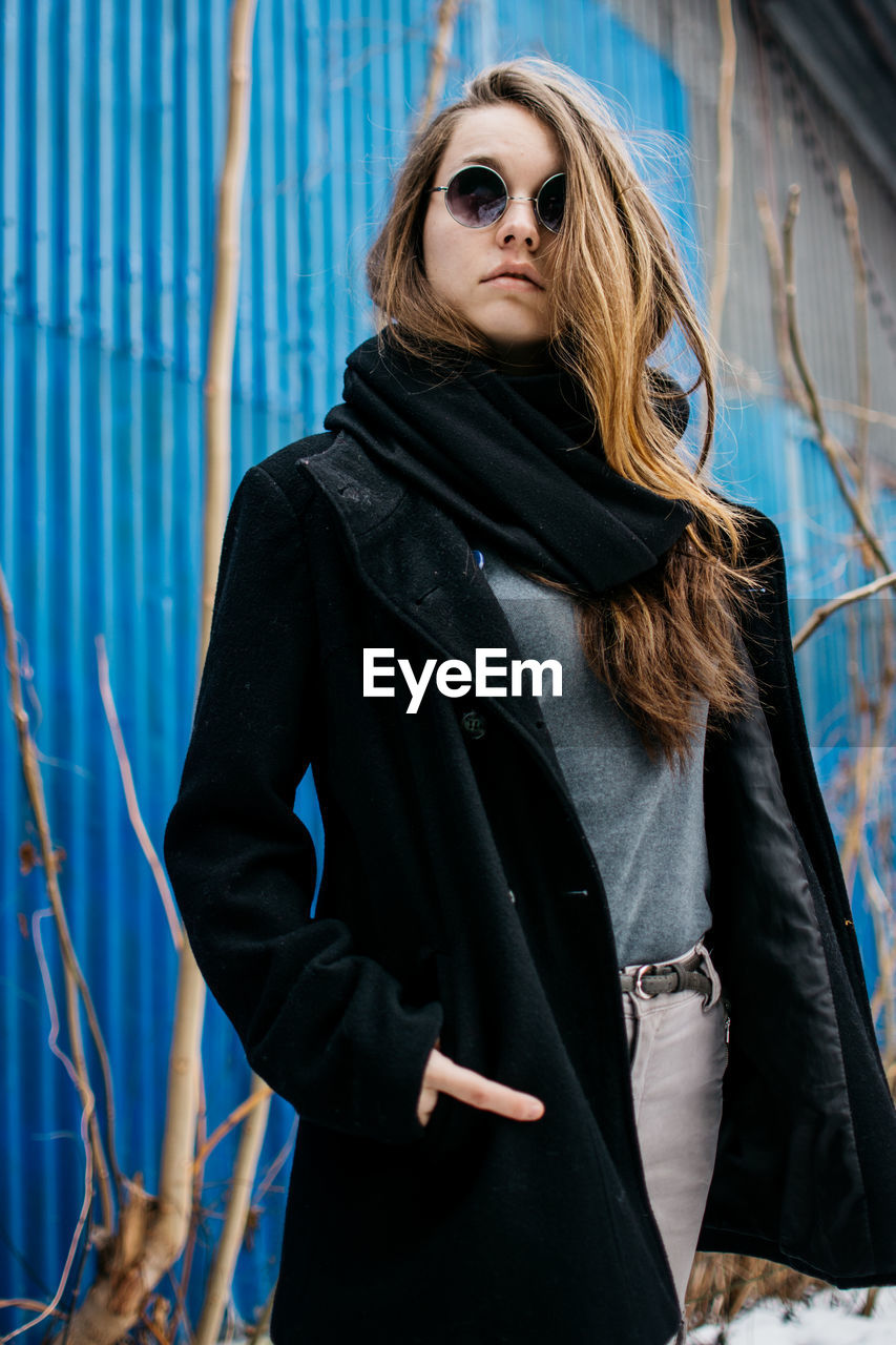 Portrait of young woman wearing warm clothing against corrugated iron