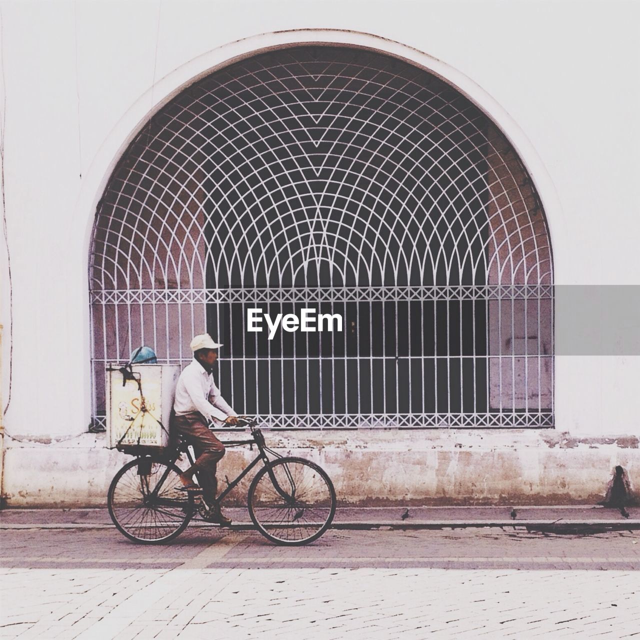Side view of man bicycling on road against arched wall