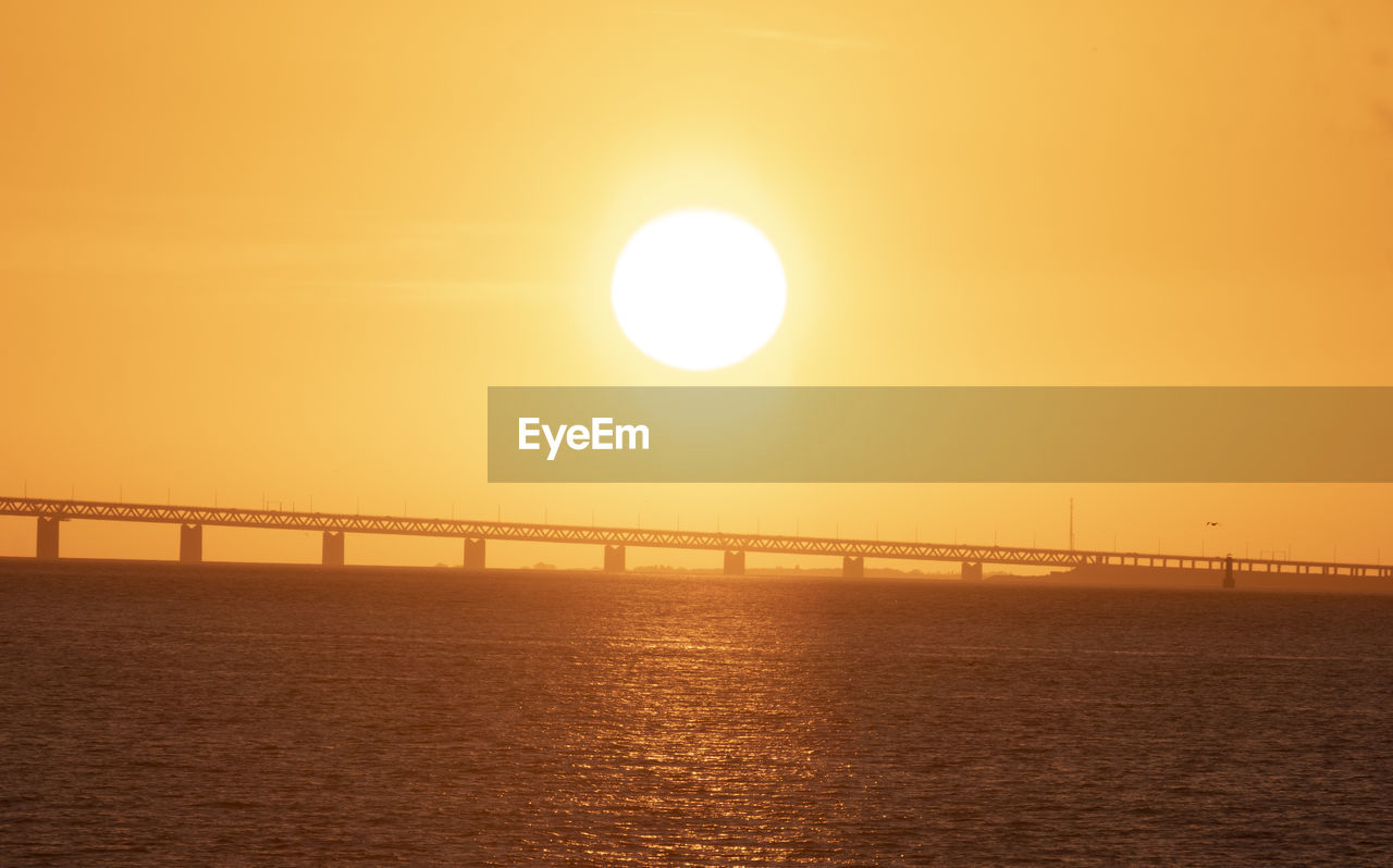 Pier over sea against orange sky