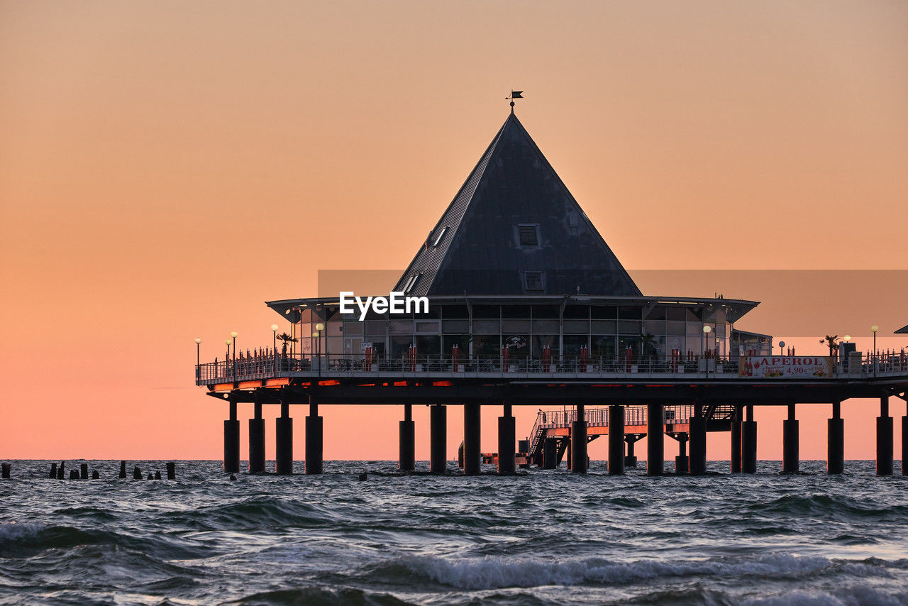 sunset, architecture, water, sky, built structure, evening, sea, dusk, ocean, horizon, nature, building exterior, pier, tower, travel destinations, beauty in nature, reflection, beach, building, no people, landmark, travel, coast, land, twilight, horizon over water, scenics - nature, outdoors, religion, orange color, history, tranquility