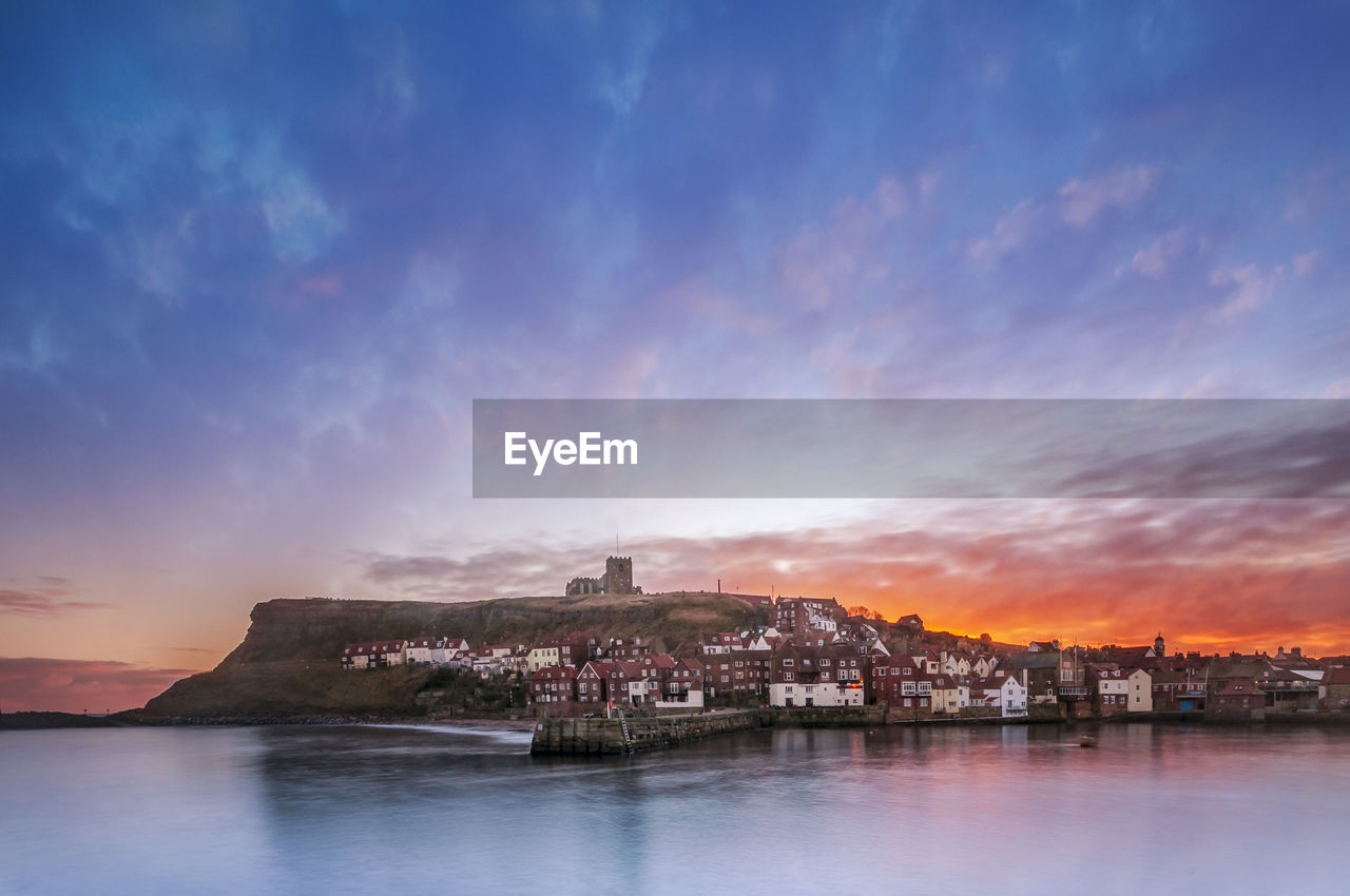 Scenic view of sea by buildings against sky at sunset