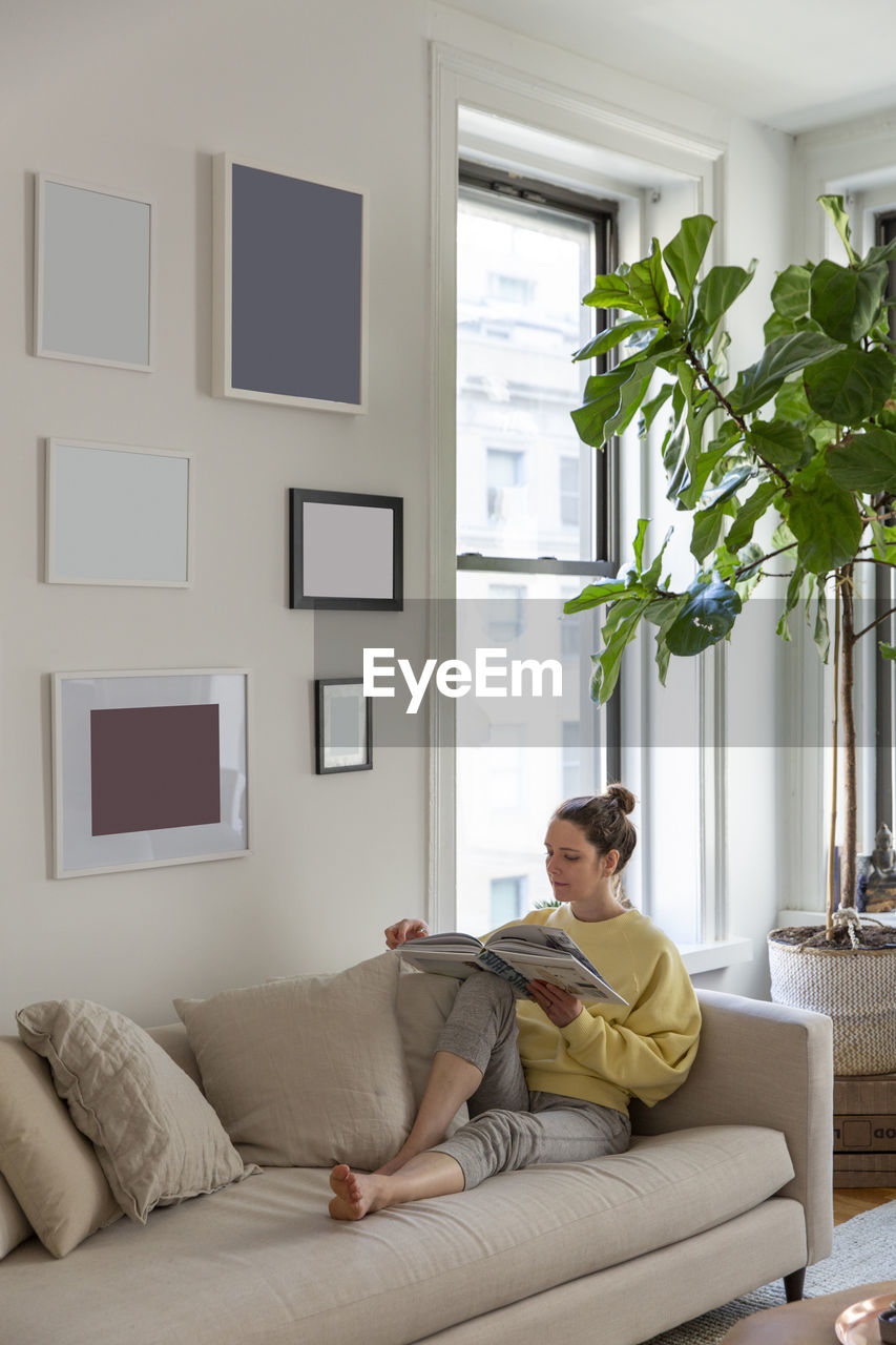 Woman reading magazine while relaxing on sofa at home