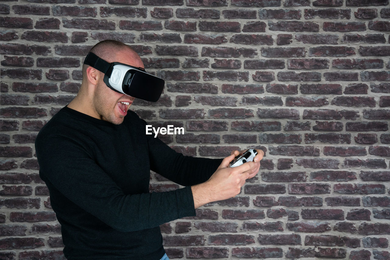 Man wearing virtual reality simulator against brick wall