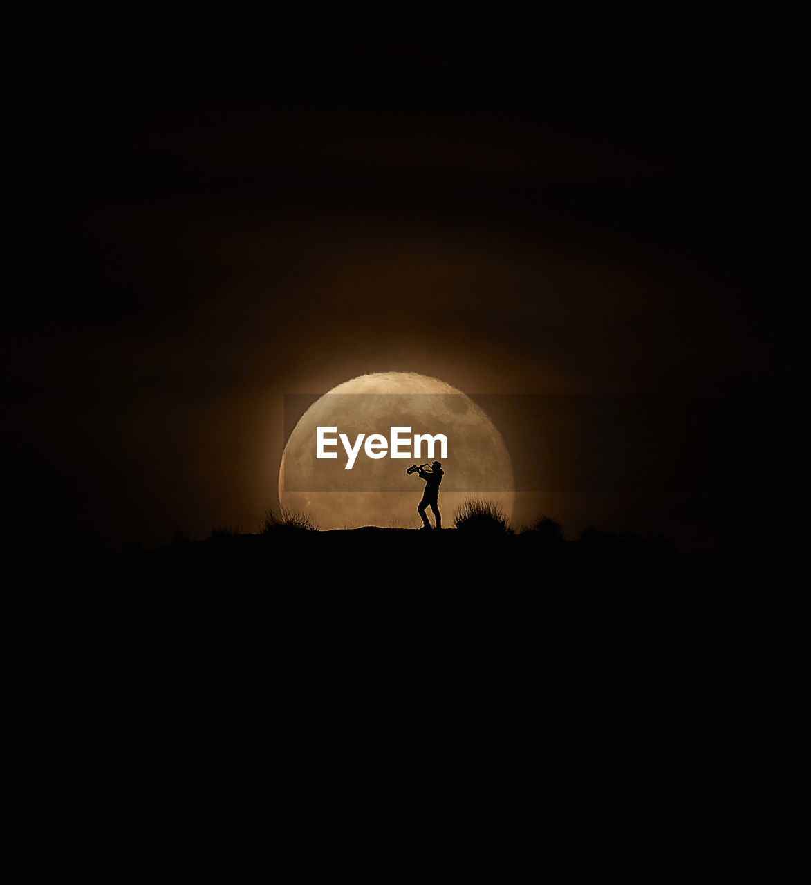 Silhouette saxophonist man against moon in sky at night