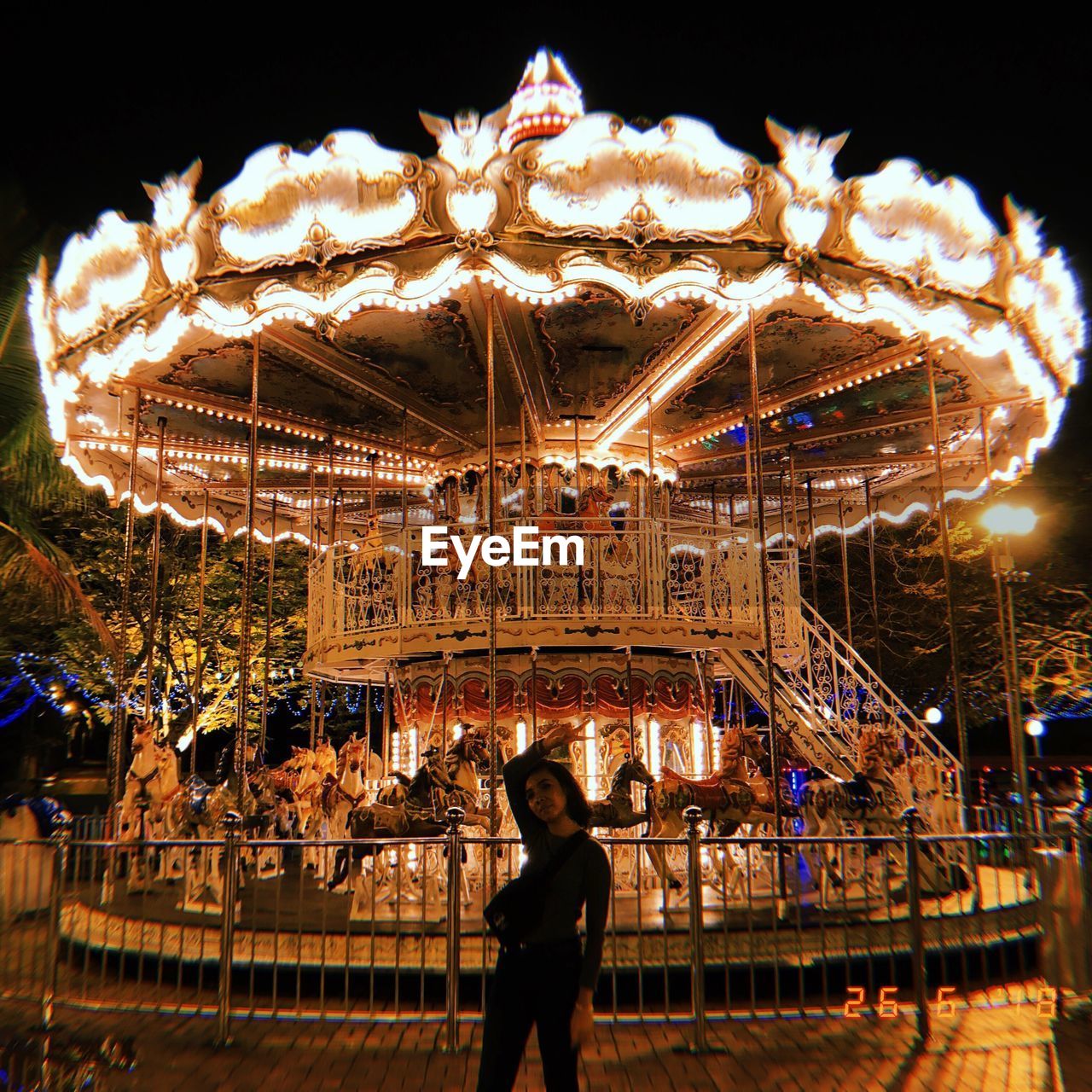 Young woman standing against illuminated carousel in amusement park at night
