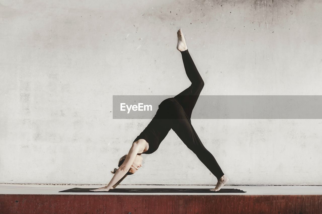 Side view of woman exercising against wall