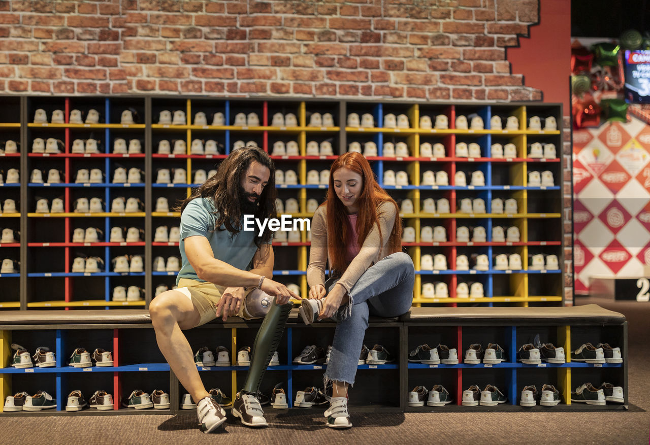 Man helping young woman tying shoes at bowling alley