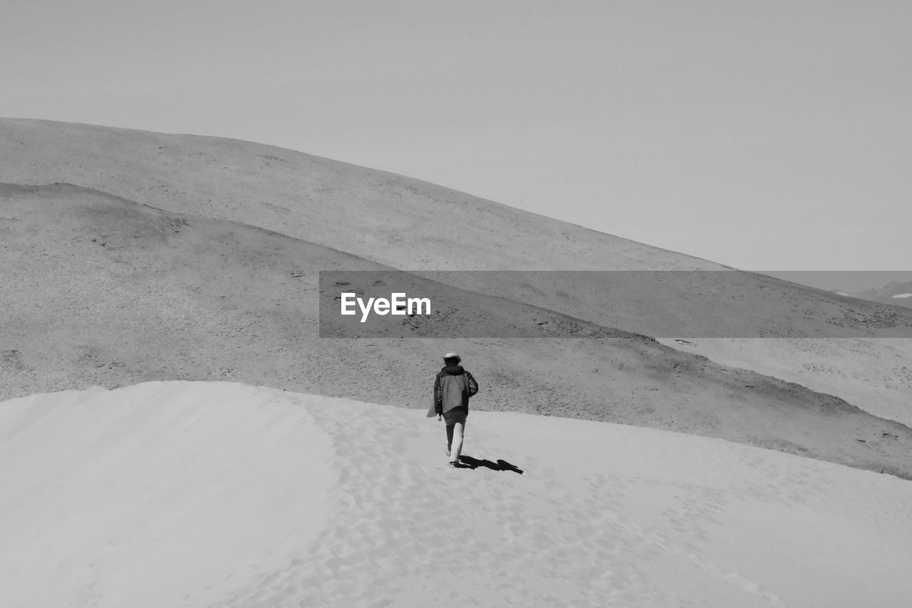 Rear view of person walking on sand at desert against clear sky