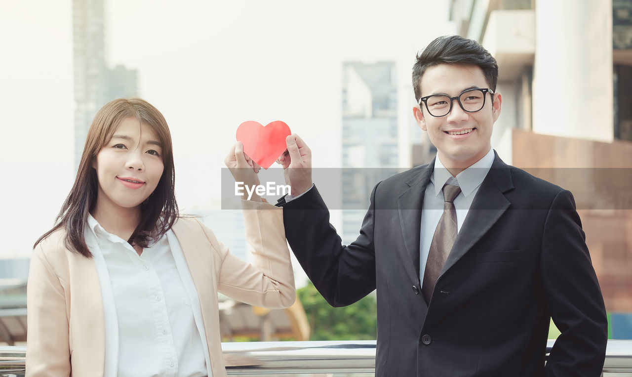 Smiling young business couple holding red paper heart shape