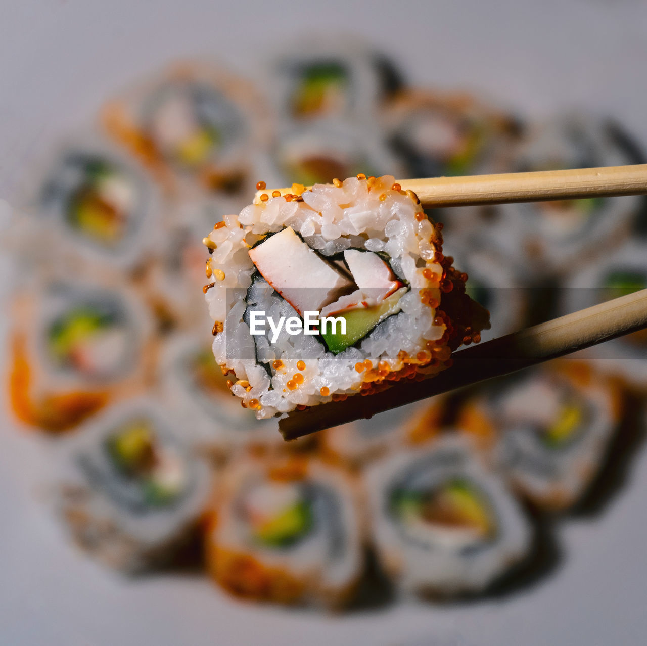 Close-up of piece of sushi held against blurred plate.