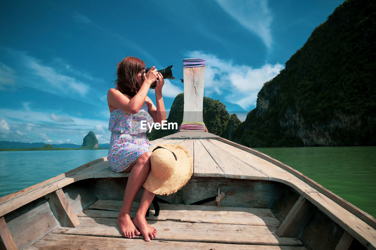 Woman photographing while sitting in rowboat against sky