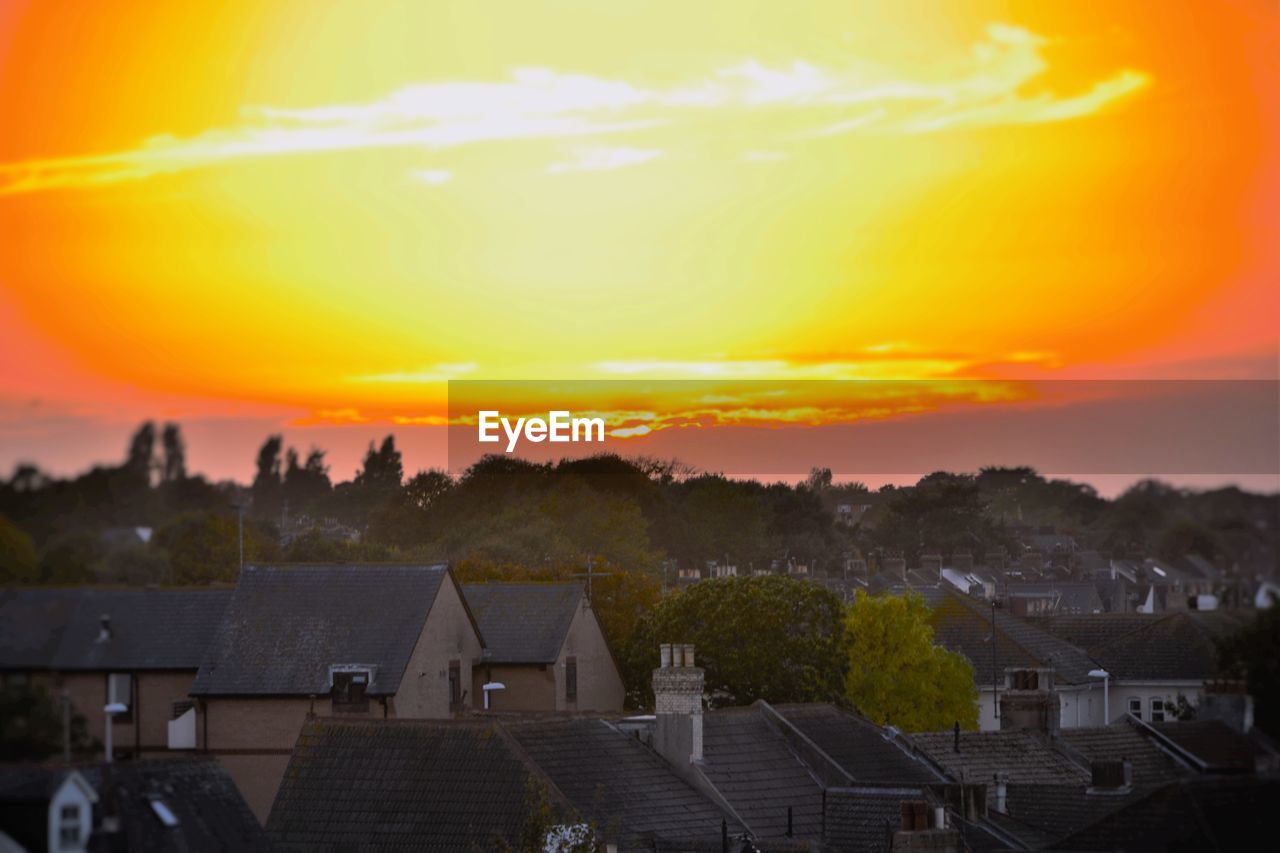 HIGH ANGLE VIEW OF HOUSES AND TREES AGAINST ORANGE SKY