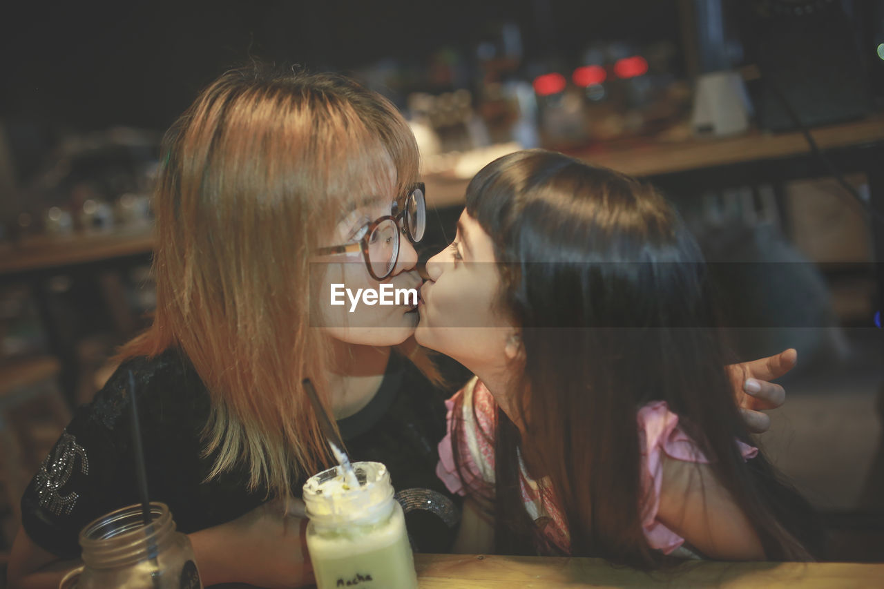 Mother kissing daughter while sitting at cafe