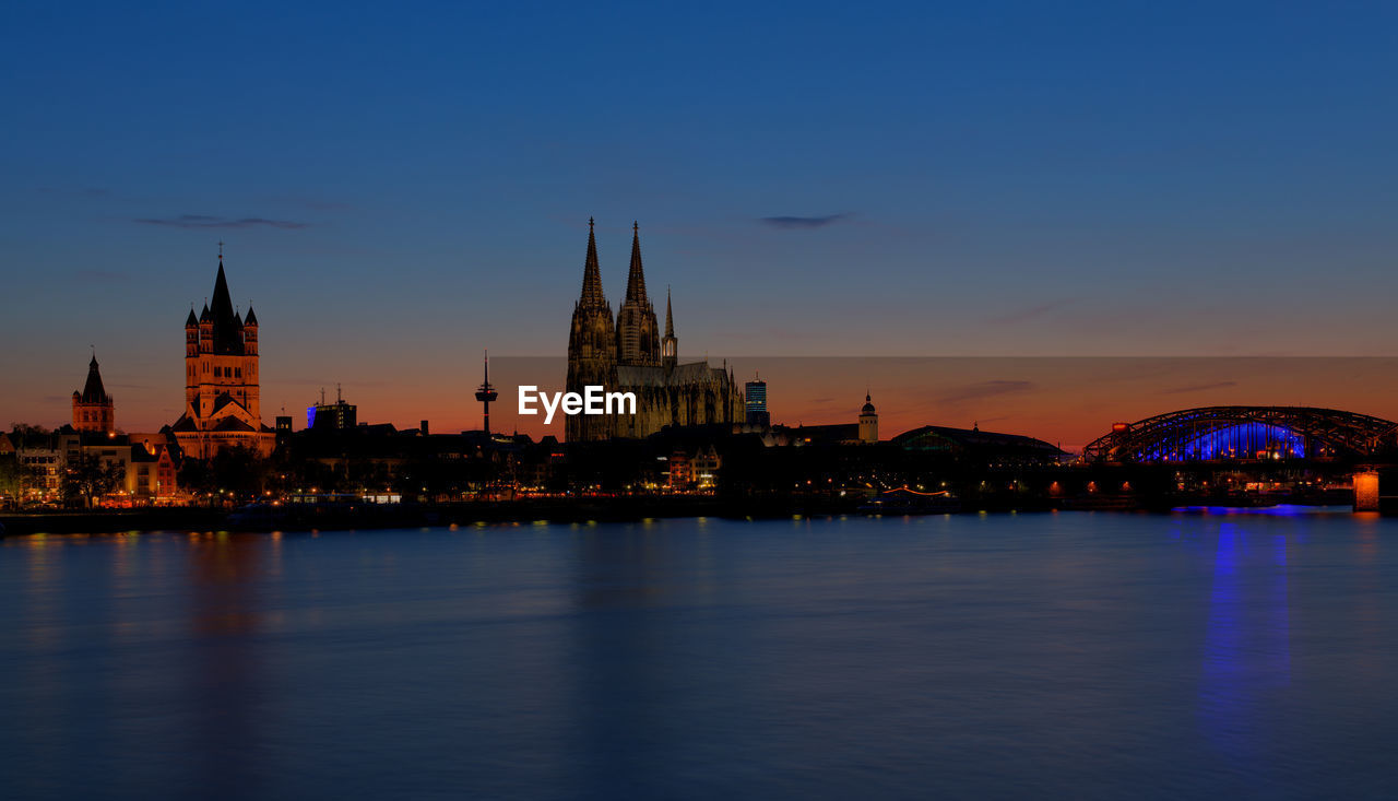 Buildings and cologne cathedral by rhine river in city at night
