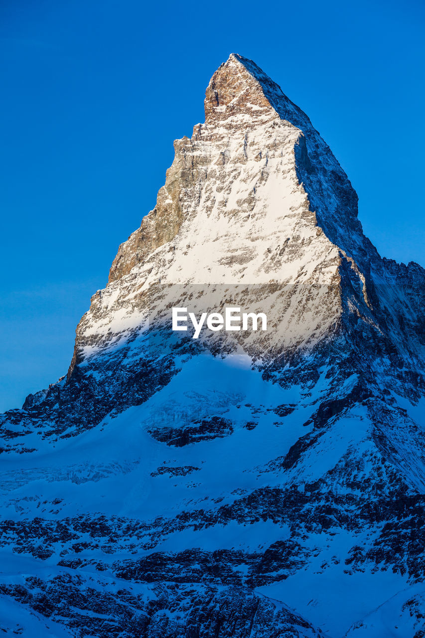 Low angle view of snow covered mountain against blue sky