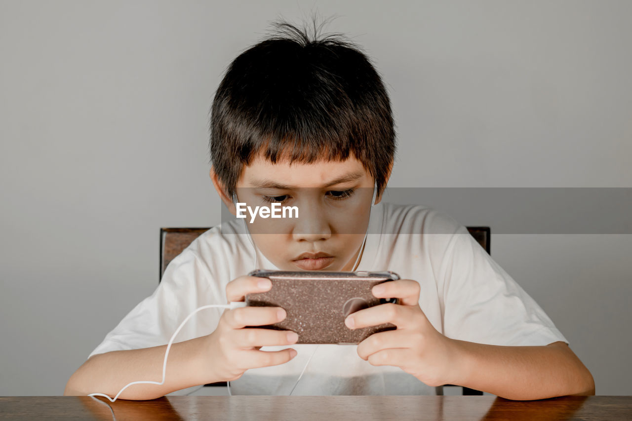 Closeup of a boy's face wearing headphones and intending to play games on his smartphone.