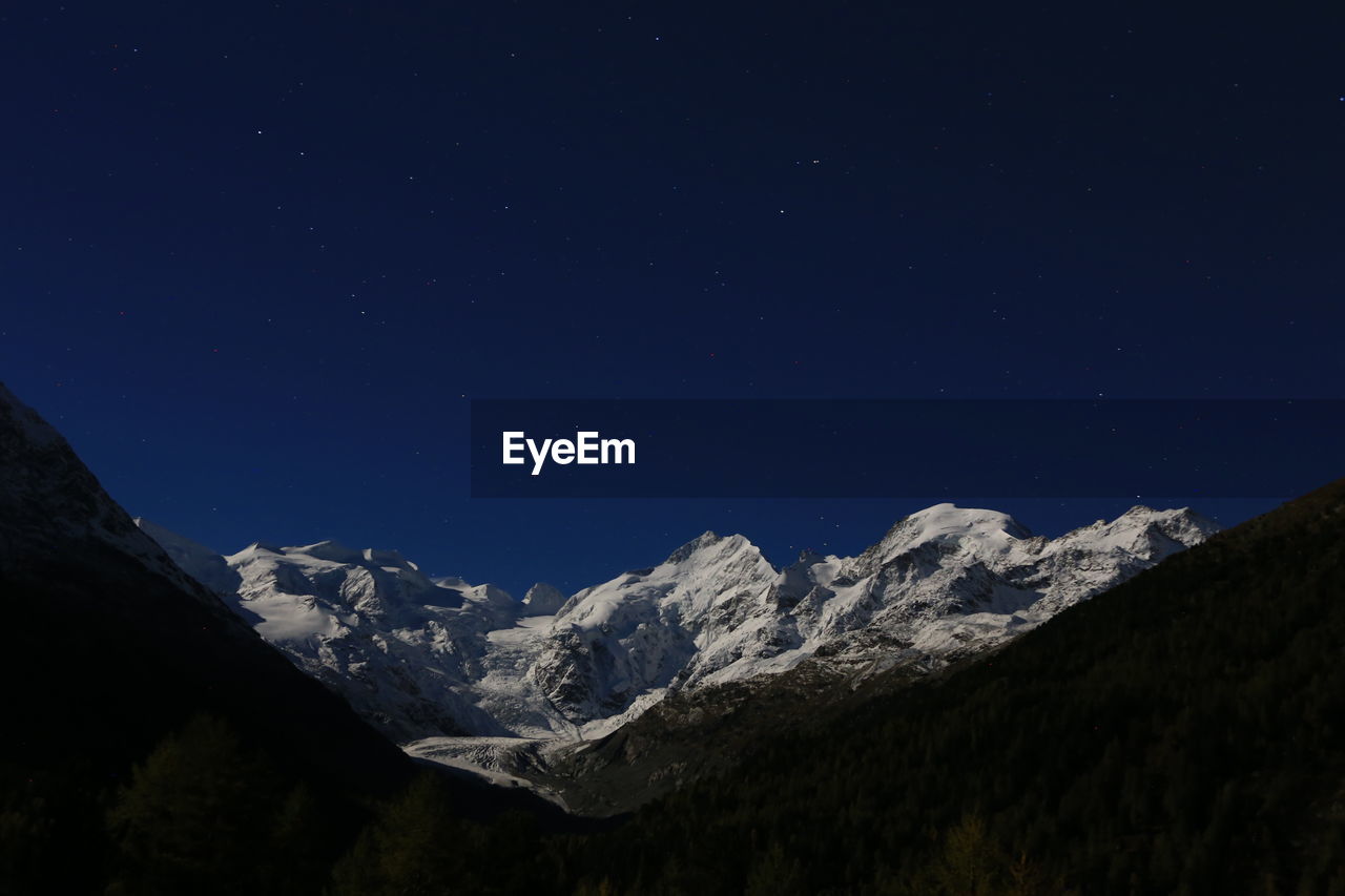 Low angle view of snowcapped mountains against sky at night