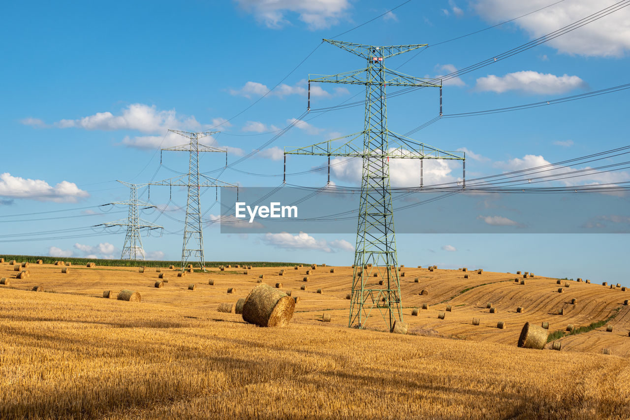 HAY BALES ON FIELD BY ELECTRICITY PYLON AGAINST SKY