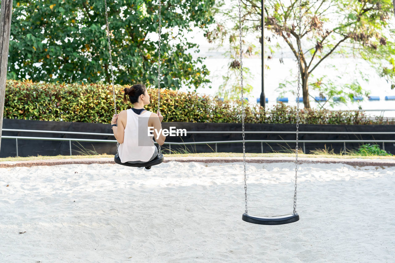 FULL LENGTH REAR VIEW OF WOMAN SITTING ON BENCH IN SWIMMING POOL