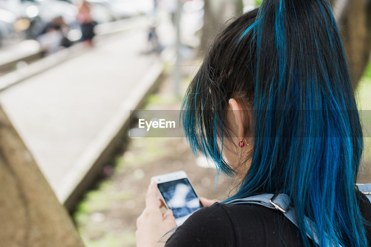 View of the back of a beautiful young blue-haired university student looking at her social networks
