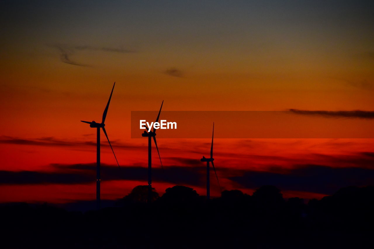 SILHOUETTE OF WIND TURBINES AGAINST ORANGE SKY