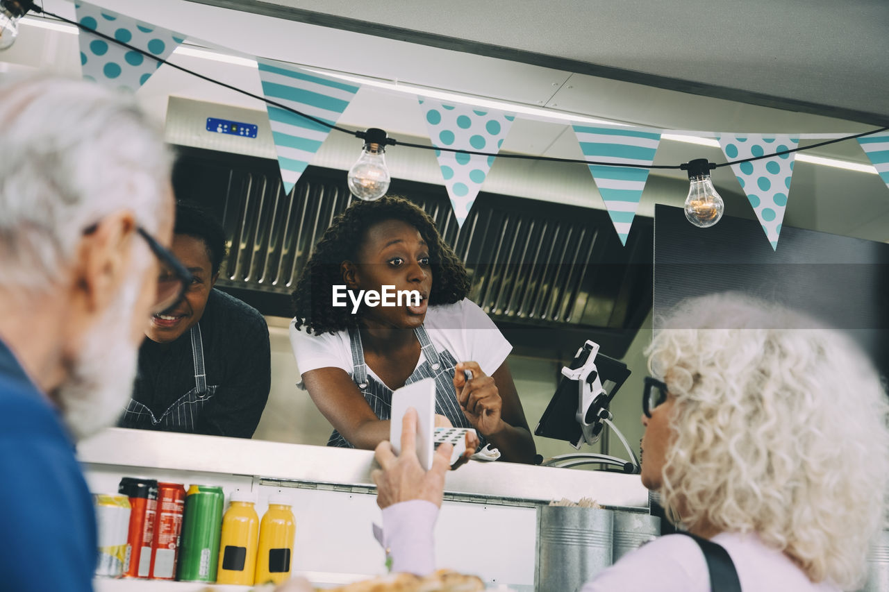 Female owner talking to customer about mobile payment while standing in food truck