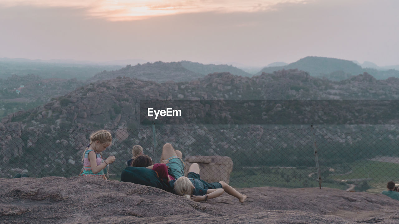 PEOPLE SITTING ON MOUNTAIN AGAINST MOUNTAINS