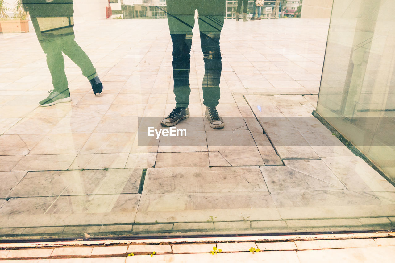 Low section of people standing against glass building