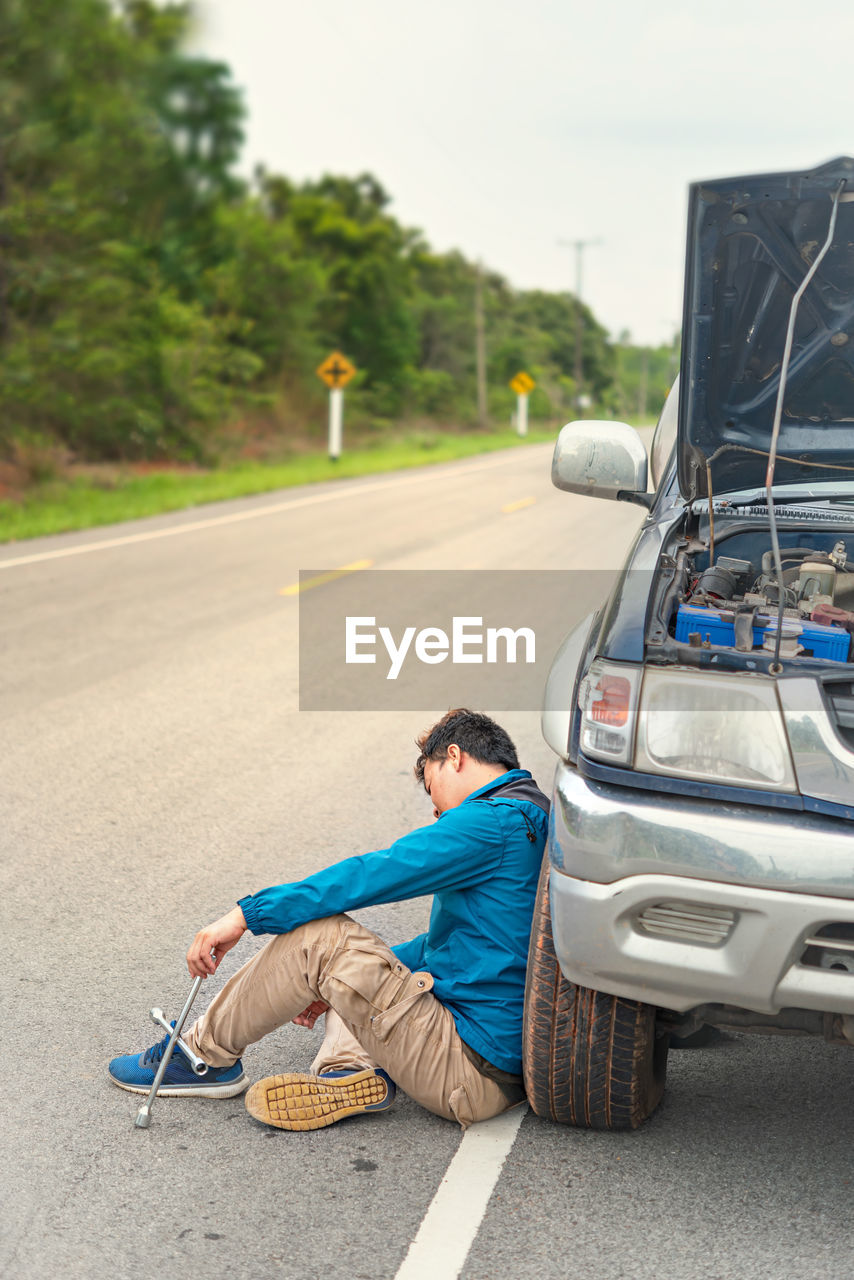 Man sitting by broken down car on road