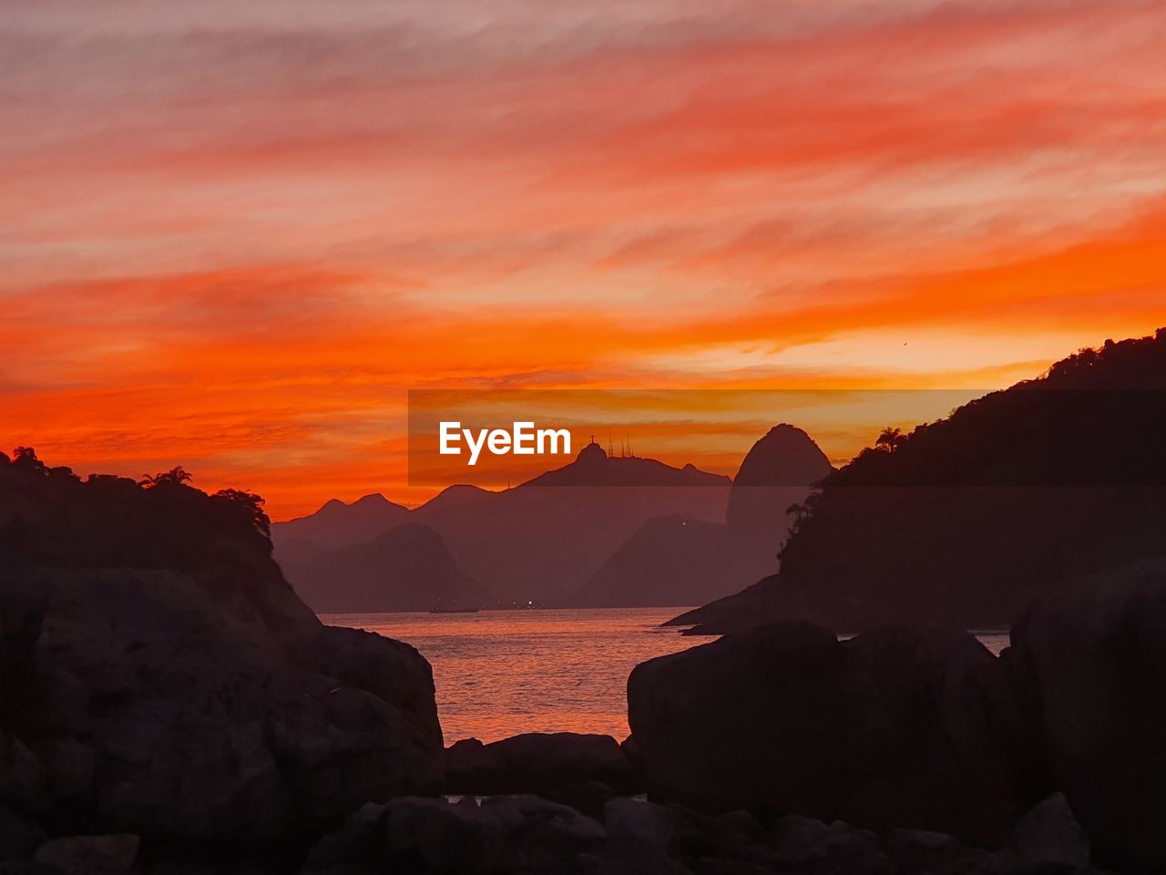 ROCKS BY SEA AGAINST ORANGE SKY