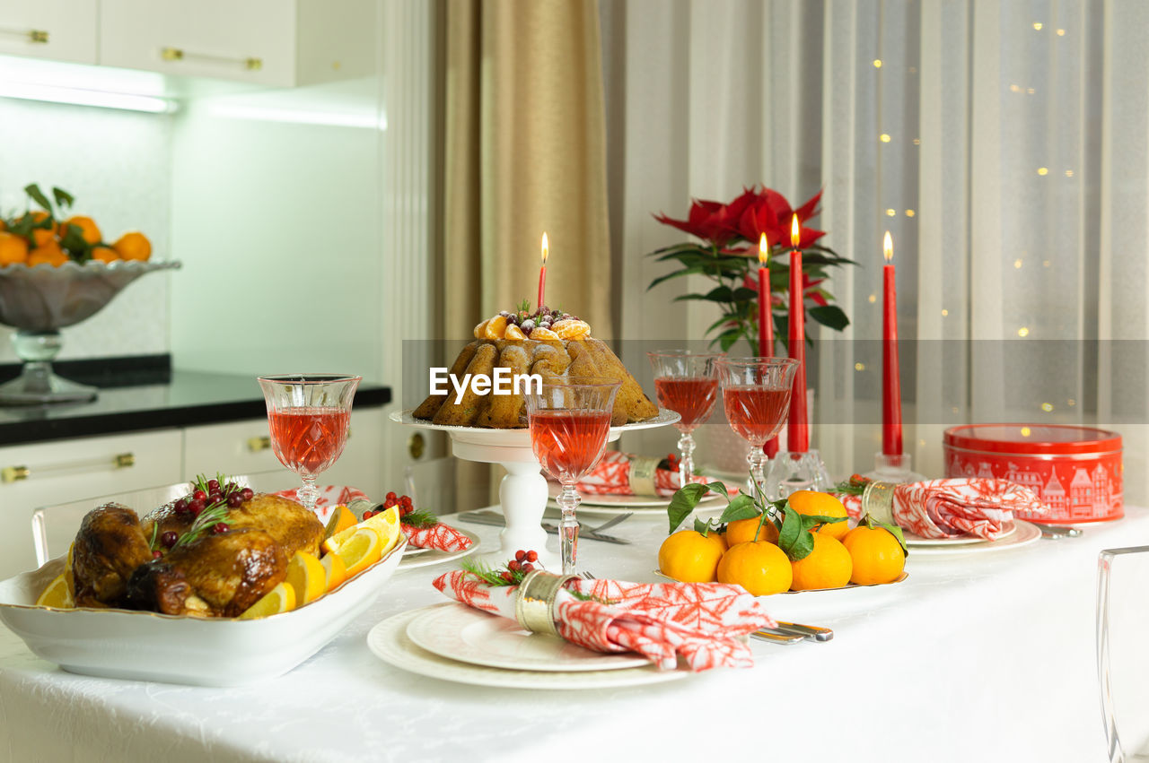 A festive table with baked chicken, tangerines, candles, cake and glasses of wine. holiday.