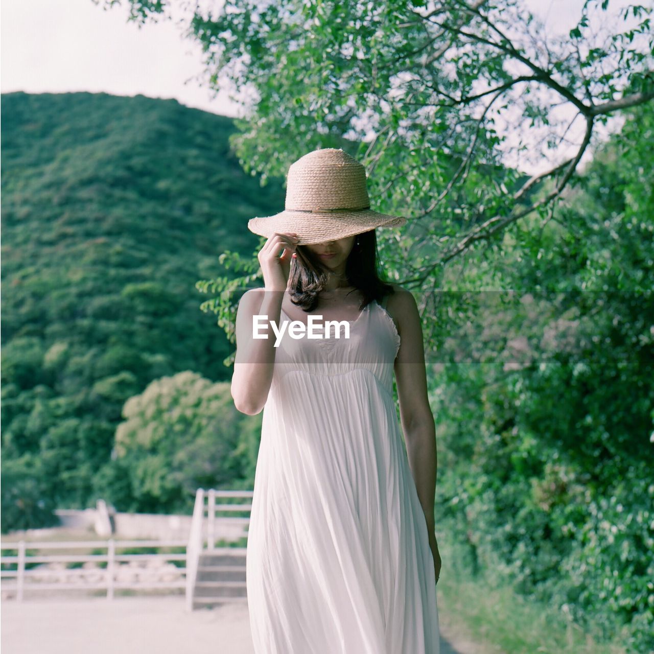 REAR VIEW OF YOUNG WOMAN STANDING AGAINST TREES