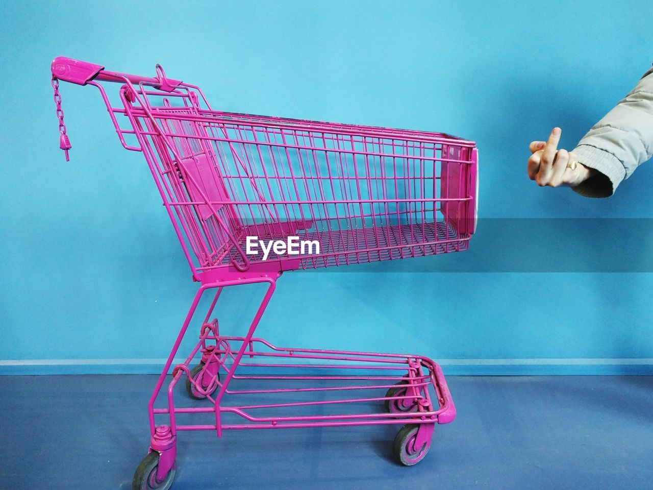 Cropped image of person showing middle finger by shopping cart against wall