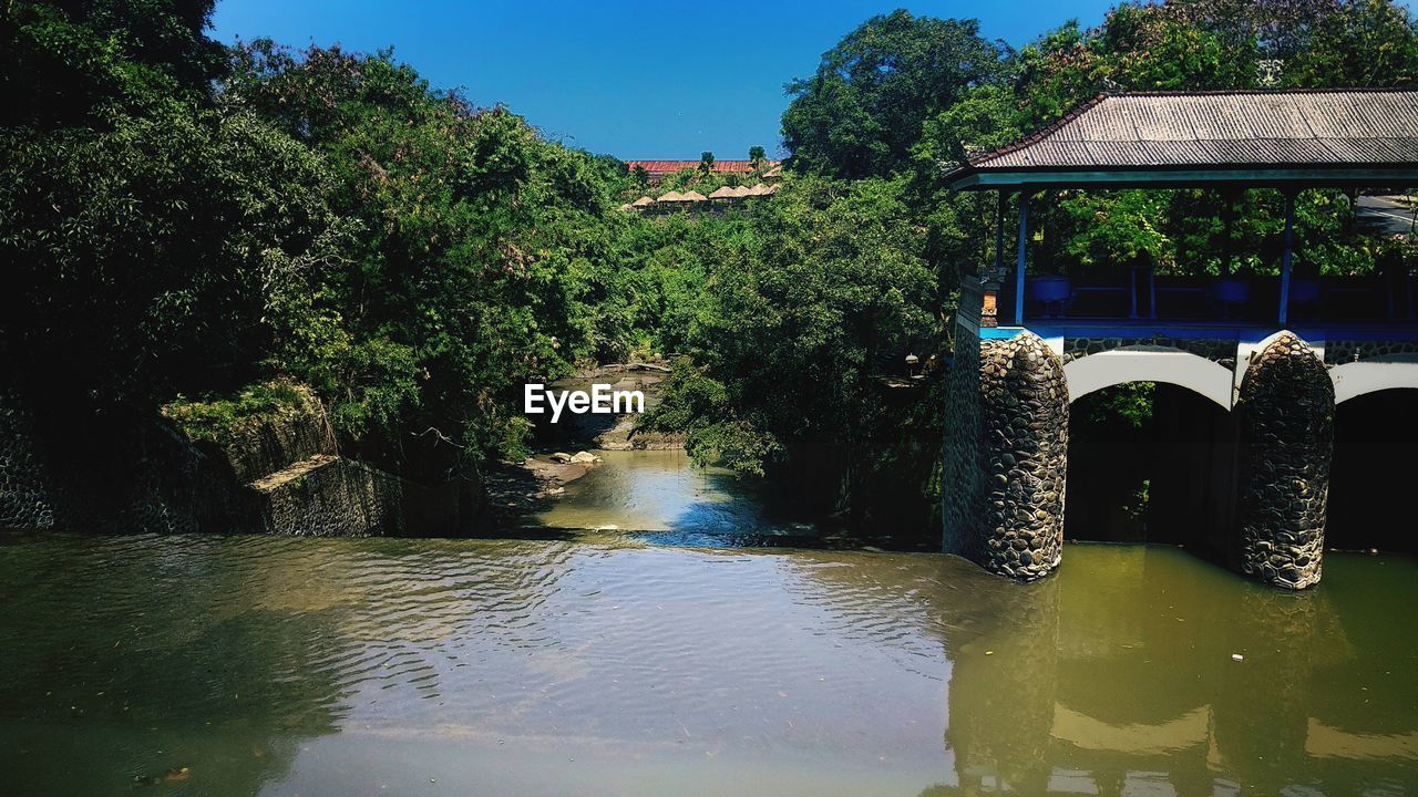 Scenic view of river by trees and building against sky