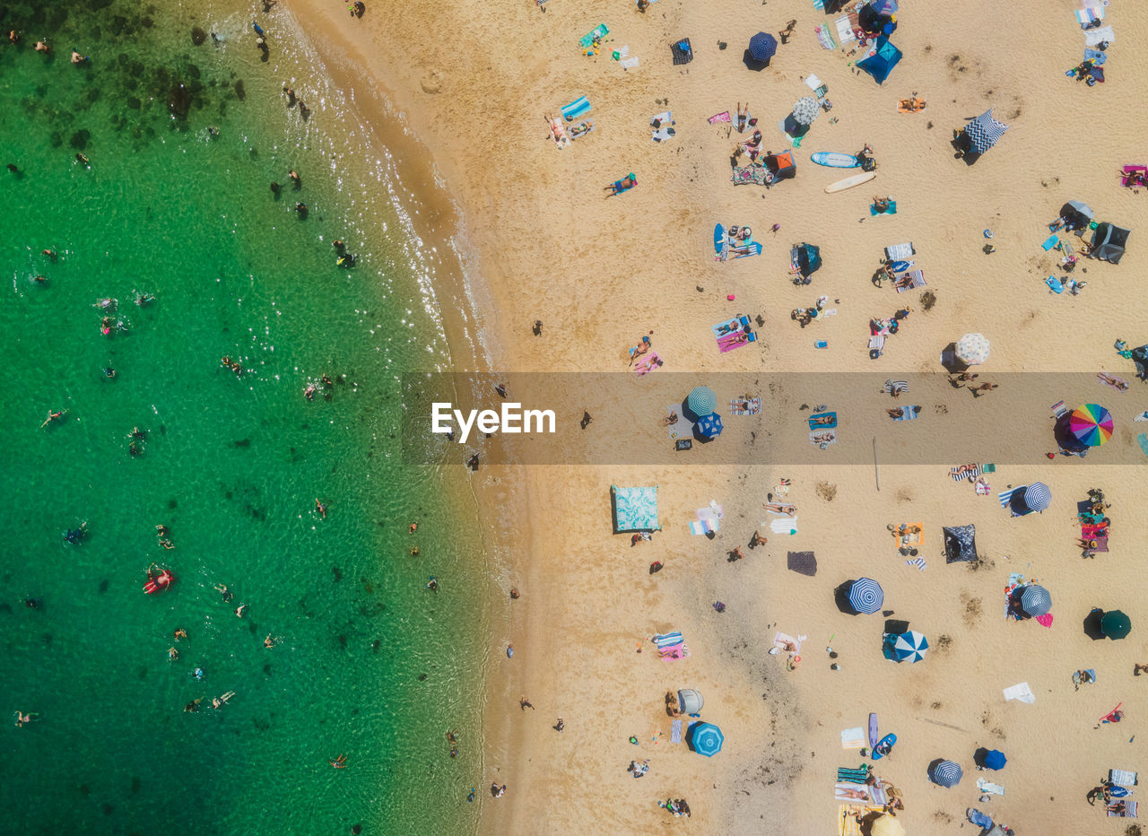Top view drone aerial of lively sandy beach with turquoise waters during a sunny summer day.